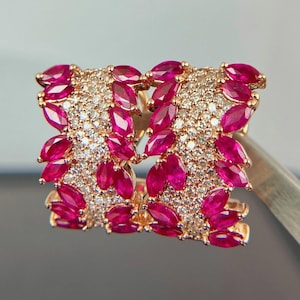 May include: A pair of gold earrings with a cluster of red ruby and white diamond stones. The earrings are shaped like a leaf and have a polished finish.