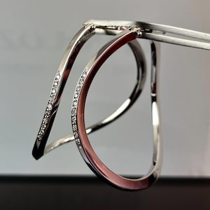 May include: Two silver bracelets with a curved design. Each bracelet is accented with a row of small, clear diamonds.