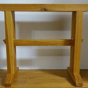 Puede incluir: Una mesa de madera simple con un acabado natural. La mesa tiene una tapa rectangular y cuatro patas. Las patas están unidas por una viga de soporte horizontal.