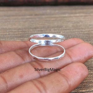 Könnte beinhalten: Ein silberner Doppelring mit gehämmertem Muster. Der Ring besteht aus zwei verbundenen Bändern, jeweils mit einer facettierten Oberfläche. Der Text "SilverBigMagic" ist unten im Bild zu sehen.