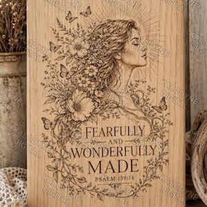 Puede incluir: Una placa rectangular de madera clara con una ilustración grabada con láser de una persona de perfil rodeada de flores y mariposas. El texto dice FEARFULLY AND WONDERFULLY MADE PSALM 139:14 en una fuente con serifa.