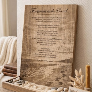 May include: Wooden plaque with the poem "Footprints in the Sand" and a beach scene. The plaque is displayed on a wooden tray filled with sand, pebbles, and seashells. A candle and a sign that says "Handcrafted with Faith & Love" are also present.