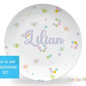 May include: White ceramic plate with a bee and honeycomb design. The plate has the name "Lilian" written in purple on it.