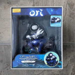 May include: A boxed 9-inch PVC painted statue of Ori and Naru, Night Edition. The figure is primarily blue with white accents and is in a seated position. The box features the text "ORI AND NARU" and "NIGHT EDITION". The box also has a sticker that says "LIGHT-UP FUNCTION".