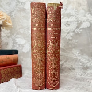 K&ouml;nnte beinhalten: Zwei antike B&uuml;cher, "Henry the Fourth" von G.P.R. James, B&auml;nde I und II, werden gezeigt. Die B&uuml;cher haben einen rotbraunen Einband mit goldenen, verzierten Designs und Schriftz&uuml;gen. Die Buchr&uuml;cken zeigen Titel und Autor. Die B&uuml;cher stammen von Harper & Brothers.