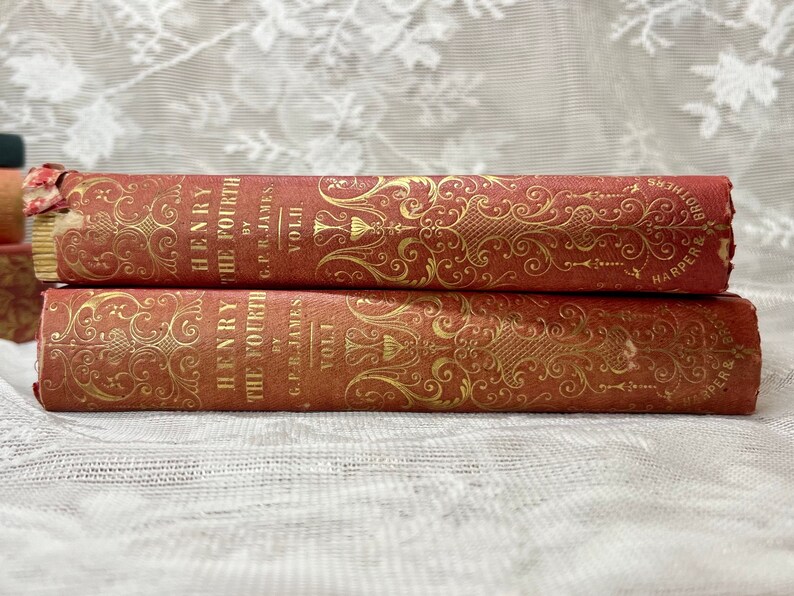 K&ouml;nnte beinhalten: Zwei antike B&uuml;cher mit dem Titel "Henry the Fourth" von G.P.R. James, Bd. I und Bd. II. Die B&uuml;cher haben einen roten Einband mit goldenen Verzierungen und Text. Der Verlag ist Harper & Brothers.