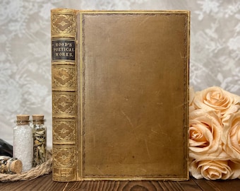 May include: A vintage, gold-colored book with the title "HOOD'S POETICAL WORKS." on the spine. The book is closed and has a worn, aged appearance.