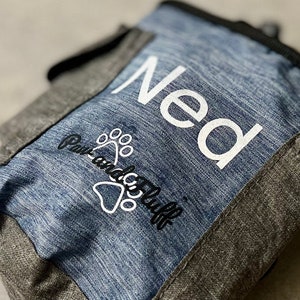 May include: A blue and grey dog treat pouch with the name "Ned" and the logo "Paw and Claws" embroidered on the front.