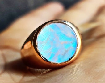 Puede incluir: Un anillo de oro con una gran piedra de ópalo azul iridiscente redonda.