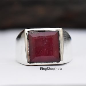 Peut inclure: Une bague en argent avec une pierre précieuse carrée rouge foncé. La bague a un design simple et classique.