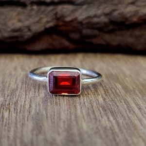 May include: A silver ring with a red gemstone set in a rectangular shape.