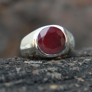 May include: A silver ring featuring a large, round, red ruby gemstone set in a bezel setting. The ring has a wide band.