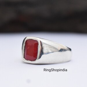 May include: A silver ring featuring a red gemstone. The ring has a simple, classic design.