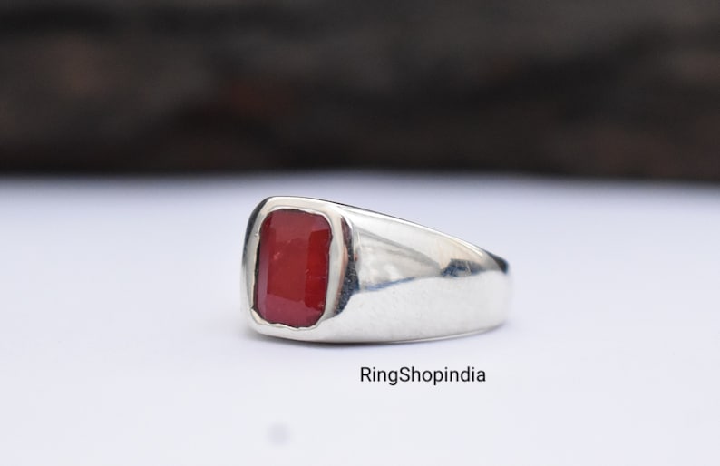 May include: A silver ring featuring a red gemstone. The ring has a simple, classic design.
