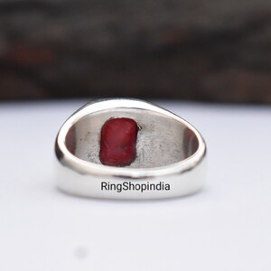 May include: A silver ring with a red gemstone set in the centre. The ring is engraved with the text "RingShopIndia".
