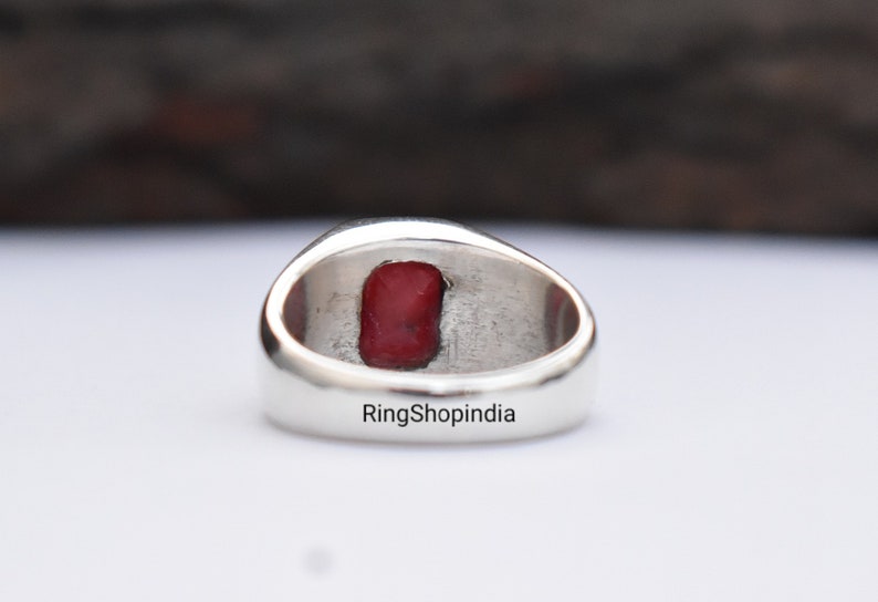 May include: A silver ring with a red gemstone set in the centre. The ring is engraved with the text "RingShopIndia".