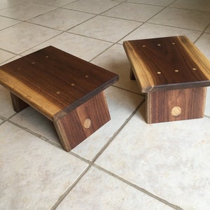 May include: Two wooden stools made of walnut wood with brass accents. The stools are on a tiled floor.