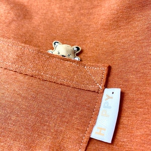 May include: A brown fabric pocket with a small embroidered animal peeking out and a white label with the word "HAPPY" on it.