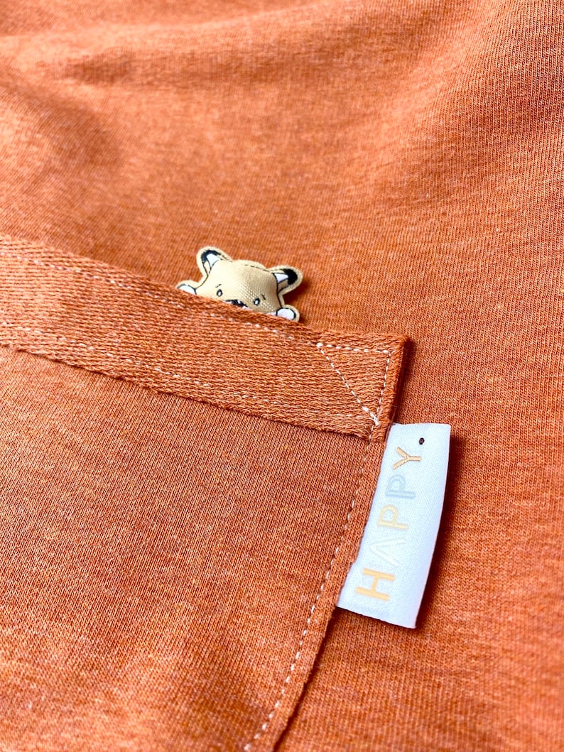 May include: A brown fabric pocket with a small embroidered animal peeking out and a white label with the word "HAPPY" on it.