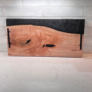 May include: A wooden serving tray with a black epoxy resin inlay. The tray has two black metal handles on the sides.
