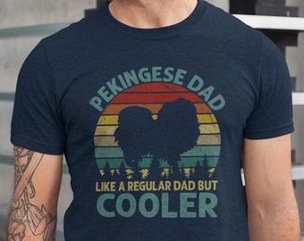 Könnte beinhalten: Ein marineblaues T-Shirt mit einer Grafik im Vintage-Stil eines Pekinese-Hundes vor einem Sonnenuntergang. Der Text "Pekingese Dad" befindet sich über der Grafik und "Like a regular dad but cooler" darunter.