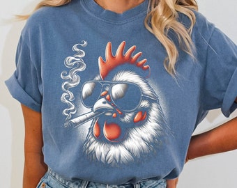 May include: A blue t-shirt with a graphic of a rooster wearing sunglasses and smoking a cigarette. The rooster has red and white feathers and a white face.