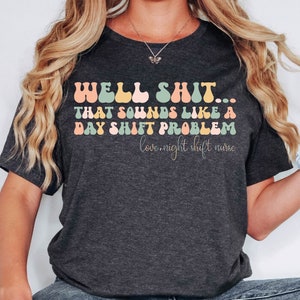 May include: A dark heather grey t-shirt with a colorful retro font graphic that reads "WELL SHIT... THAT SOUNDS LIKE A DAY SHIFT PROBLEM love, night shift nurse".