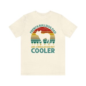 May include: A beige t-shirt with a vintage-style graphic of a French Bulldog. The graphic says "French Bulldog Dad Like a Regular Dad But Cooler".