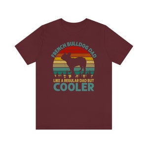 May include: A maroon t-shirt with a vintage-style graphic of a French Bulldog. The graphic says "French Bulldog Dad Like a Regular Dad But Cooler".