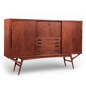 May include: A mid-century modern wooden cabinet with a rich, reddish-brown finish. The cabinet features a central section with drawers and a lock, flanked by curved doors. It stands on angled legs, showcasing a classic design.