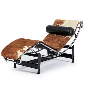 May include: A modern chaise lounge with a brown and white cowhide seat and backrest. The frame is made of black metal with chrome accents. A black leather bolster pillow provides neck support. The chair is designed for relaxation and comfort.