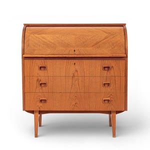 May include: A mid-century modern wooden desk with a roll-top and three drawers. The desk is made of light brown wood and has a keyhole on the roll-top. The drawers have rectangular handles and the desk has four legs.