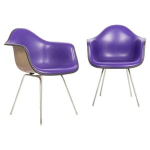 May include: Two mid-century modern chairs with purple seats and chrome legs. The chairs have a molded plastic design with a curved back and armrests. The legs are made of thin, angled metal rods.