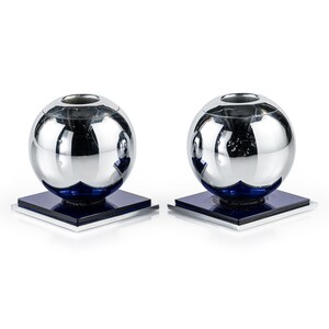 May include: A pair of candle holders featuring a spherical, reflective chrome top section resting on a deep blue square base. Each holder has a circular opening at the top and a layered square foundation with a metallic silver trim at the bottom edge.