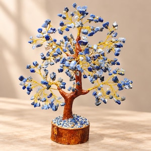Pode incluir: Uma escultura decorativa de árvore com um tronco castanho e ramos feitos de fio dourado fino. Os ramos estão adornados com numerosas pequenas pedras de sodalite azul polidas. A árvore está montada numa base redonda de madeira natural.