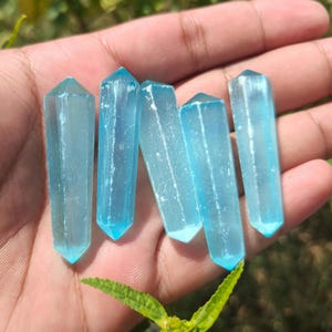 May include: Five double-terminated crystal points with a translucent light blue hue. Each piece features a hexagonal shape with pointed ends and visible internal striations, showcasing a smooth, polished surface texture throughout.