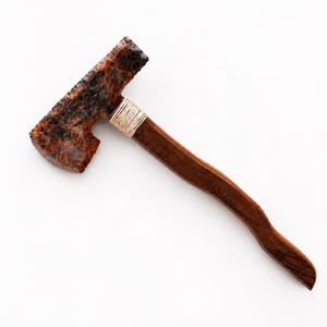 May include: A rustic axe with a dark brown wooden handle and a weathered, reddish-brown blade. The blade is wrapped with a natural-colored twine near the handle. The axe is set against a white background.