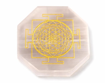 May include: A light pink selenite crystal coaster with an octagonal shape. The coaster features a gold-colored Sri Yantra design in the center. The design is a geometric pattern with a circular center and square outer edges.