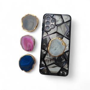 May include: A smartphone case with a geometric pattern and a natural stone accent. Three additional natural stone accents in gray, pink, and blue with gold edges are also displayed. The case and accents are on a white background.