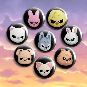 Op de afbeelding: Een verzameling van negen zwarte buttonspins met cartoon-dierengezichten. De dieren zijn een roze varken, een gele kuiken, een witte beer, een blauwe wolf, een witte konijn, een bruine hond, een bruine hamster en een lichtbruine vos. De achtergrond is een verloop van paars en oranje.