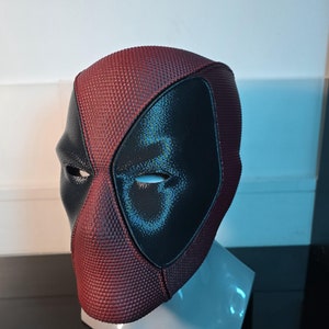 Puede incluir: Una m&aacute;scara de Deadpool roja y negra con una superficie texturizada. La m&aacute;scara tiene un &aacute;rea de ojos negra con una forma de ojo blanca.