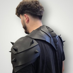 May include: Black shoulder armor with prominent, dark spikes. The armor is designed with layered plates and a spiked shoulder guard. The image shows the armor from the back, suggesting a costume or cosplay item.