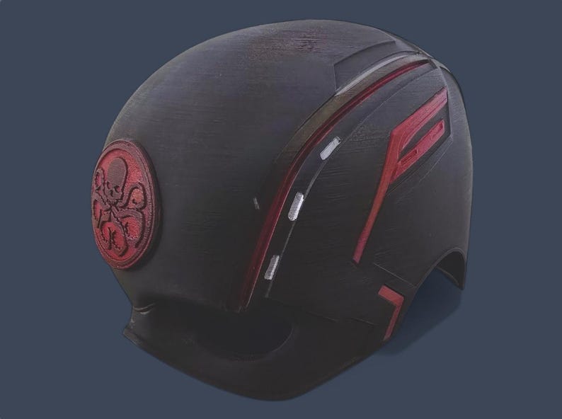 May include: A black helmet with red and white stripes and a red Hydra logo. The helmet is made of a textured material and has a slightly worn look.