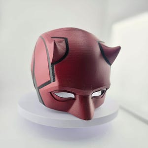 Puede incluir: Una máscara de Daredevil roja y negra con cuernos. La máscara está hecha de un material texturizado y tiene un diseño detallado.