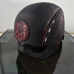 May include: Black helmet with a red Hydra logo and red and white stripes. The helmet is made of a textured material.