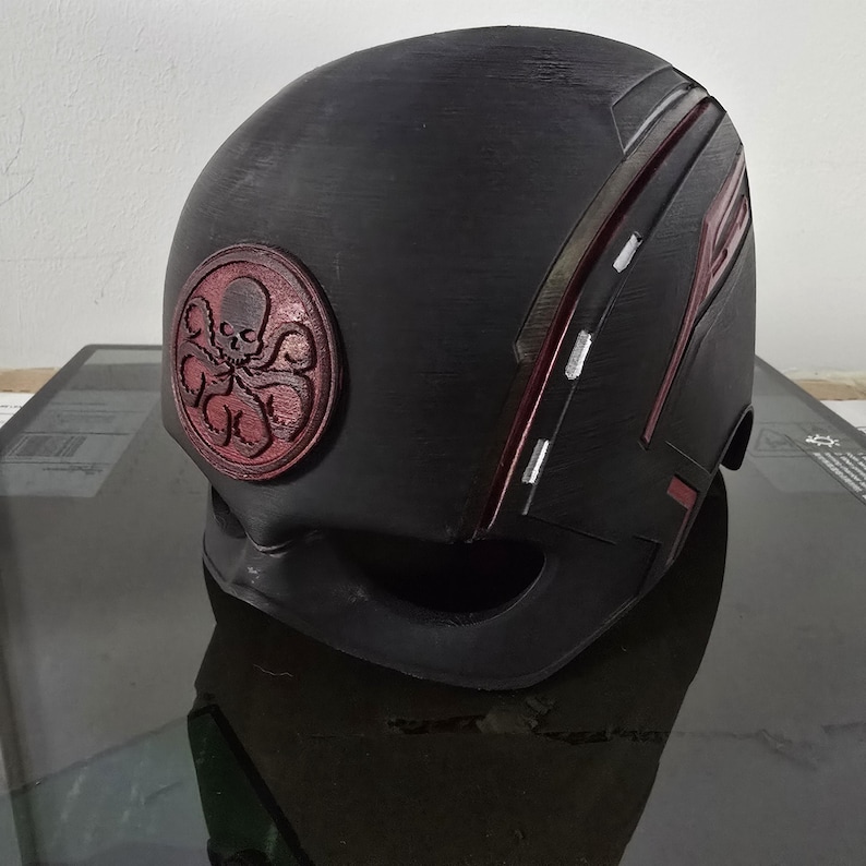 May include: Black helmet with a red Hydra logo and red and white stripes. The helmet is made of a textured material.