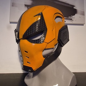 Puede incluir: Una máscara de plástico negra y naranja con un diseño de panal en el área de los ojos. La máscara tiene una superficie texturizada y está diseñada para cubrir la cara.