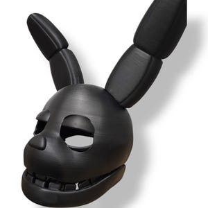 Op de afbeelding: Een zwart konijnenmasker met beweeglijke oren en een gedetailleerd ontwerp met open mond. Het masker heeft ooggaten en een gestructureerd oppervlak, waarschijnlijk 3D-geprint. De algehele esthetiek is donker en gestileerd, geschikt voor cosplay of kostuums.