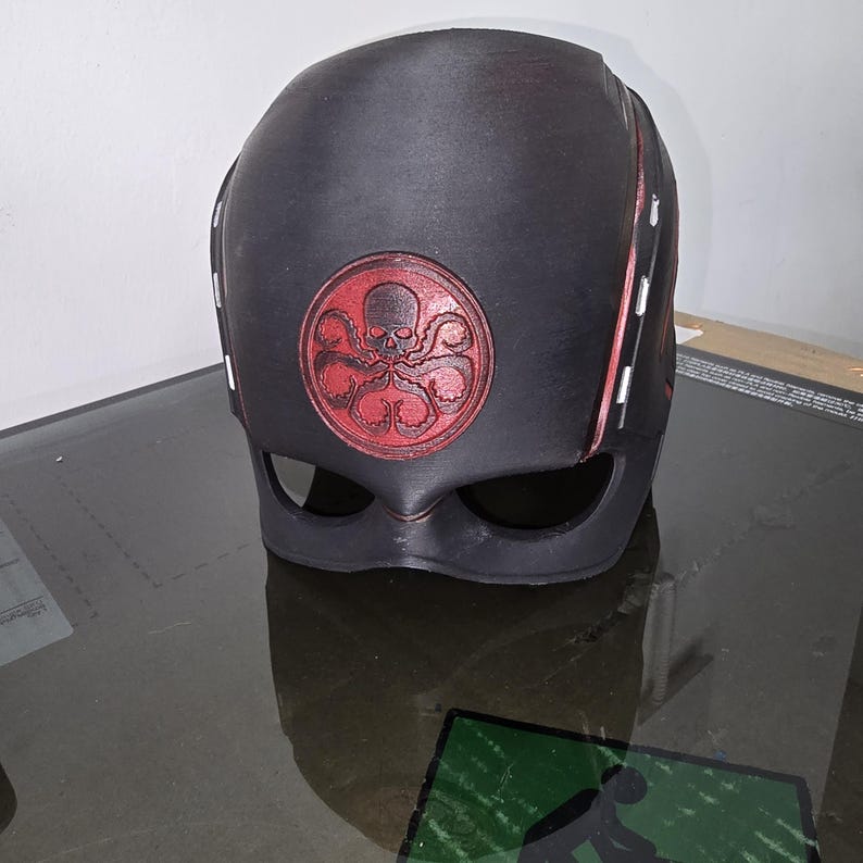 May include: A black plastic mask with a red Hydra logo. The mask features a skull and tentacles in the logo. The mask has a black visor and red accents.
