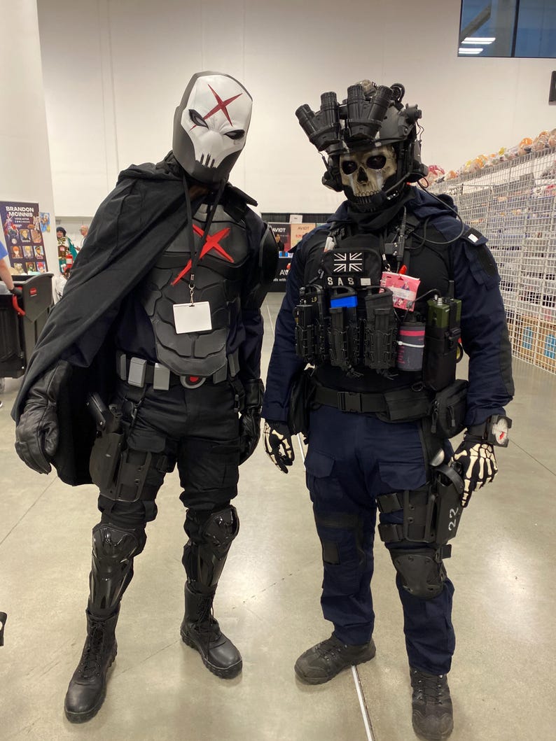 May include: Two individuals in tactical cosplay costumes. The left figure wears a white skull mask with a red X, black armor, and a cape. The right figure wears a skull mask, night vision goggles, a dark blue uniform with SAS patches, and tactical gear.
